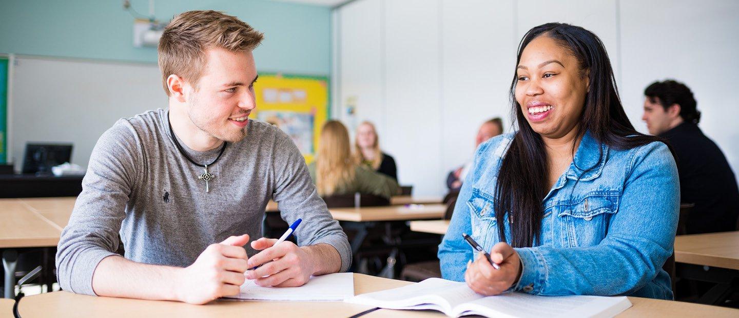 male and female sitting in a classroom at a table with open books